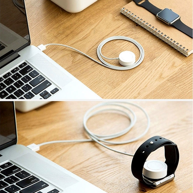 White charging puck with cable coiled near a smartwatch on a wooden desk.