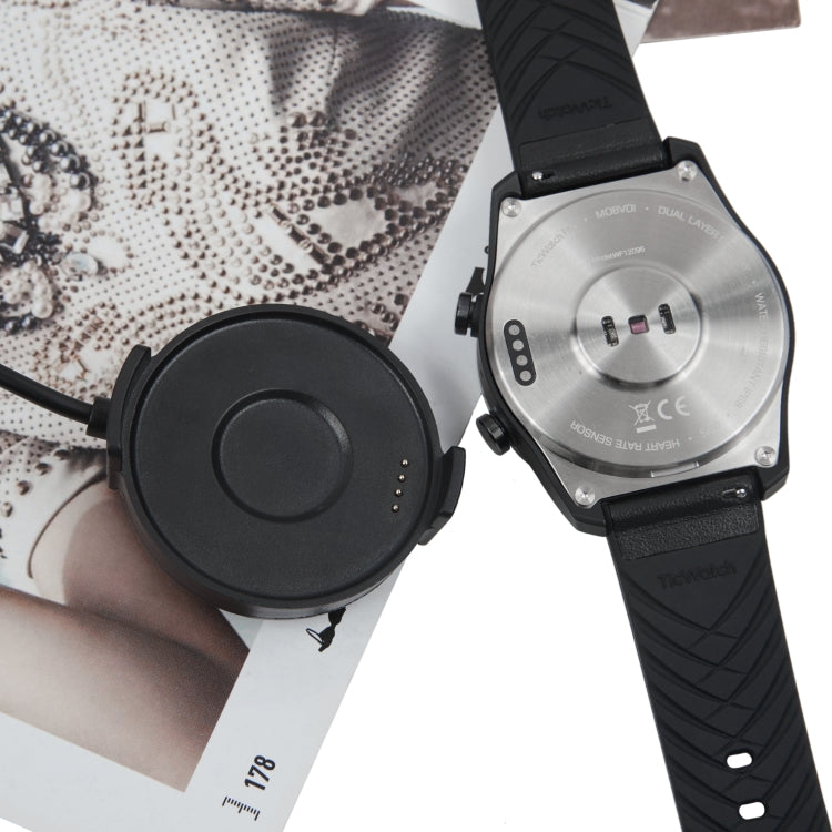 Black smartwatch on strap with charging puck and cable
