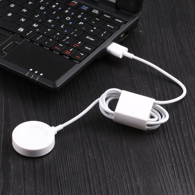 White charging puck connected by cable to USB port near a laptop keyboard