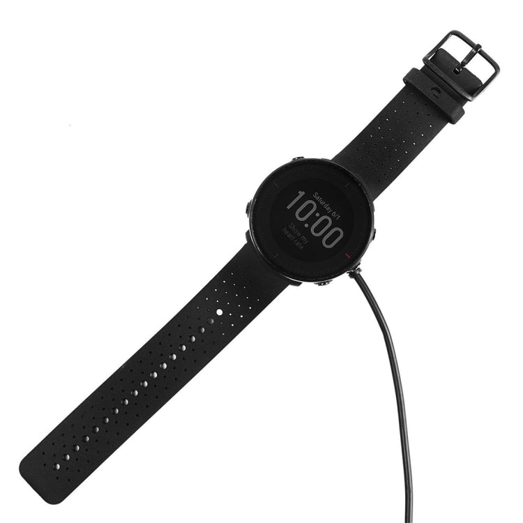 Smartwatch with black perforated band and charging cable connected to dock puck