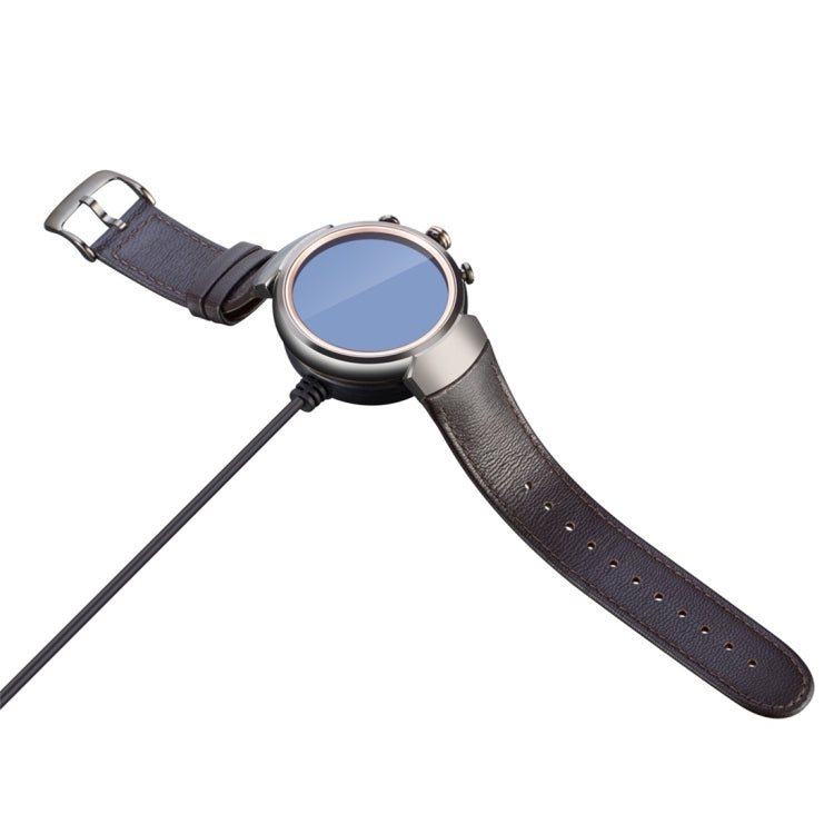 Gray smartwatch-style device with charging cable connected at the side port
