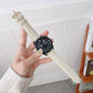 Leather watch strap in light color with perforated holes, worn on a wrist watch.