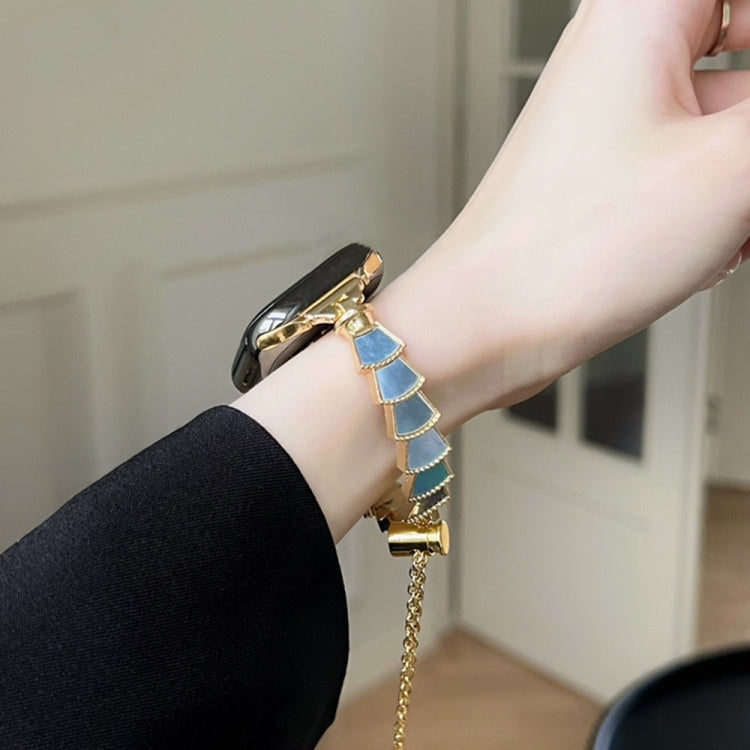 Gold-tone metal watch band with shell links and light blue inserts, close-up on wrist