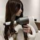 Woman styling dark hair with a hair dryer and attached curling roller nozzle.