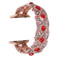 Twist metal watch band in rose gold with red crystal stones, ornate linked design.