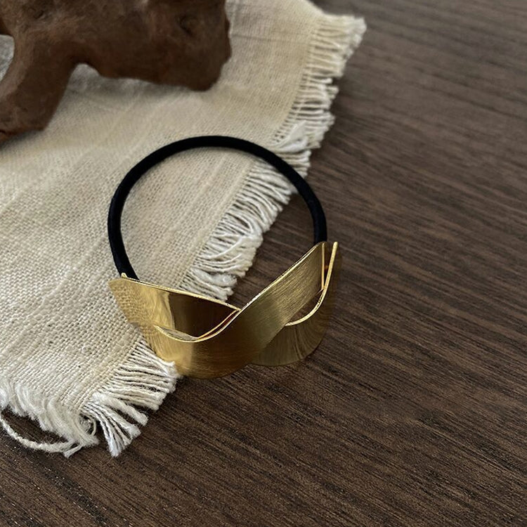 Gold metal bow hair tie with black elastic loop, close-up detail