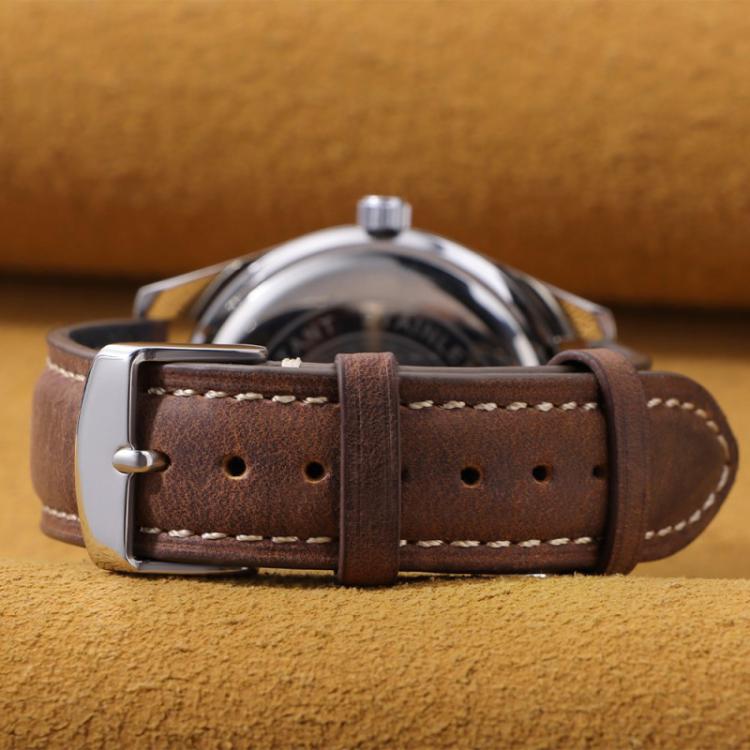 Dark brown leather watch band fastened around a watch, showing holes and buckle