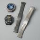 Two segmented titanium alloy watch bands in dark gray and silver, shown beside compatible watches.