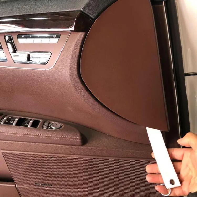 White trim removal tool held by hand near an interior panel edge