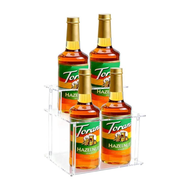 Clear acrylic 2-tier bottle organizer rack holding six Torani hazelnut syrup bottles