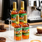 Clear acrylic 2-tier rack on countertop holding hazelnut syrup bottles
