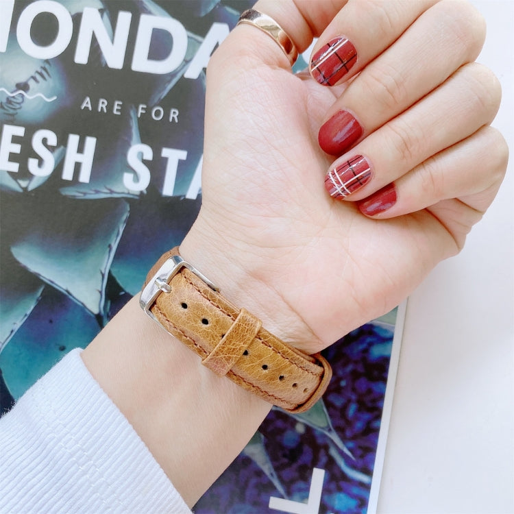 Double-sided leather watchband on wrist, tan perforated strap with metal buckle
