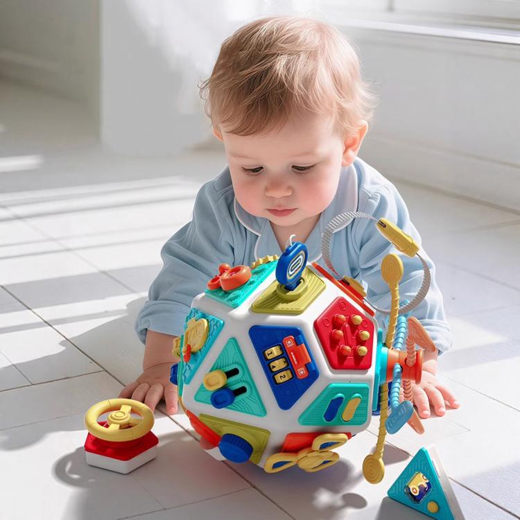 Toddler playing with a busy board cube toy with buttons, gears, and latches