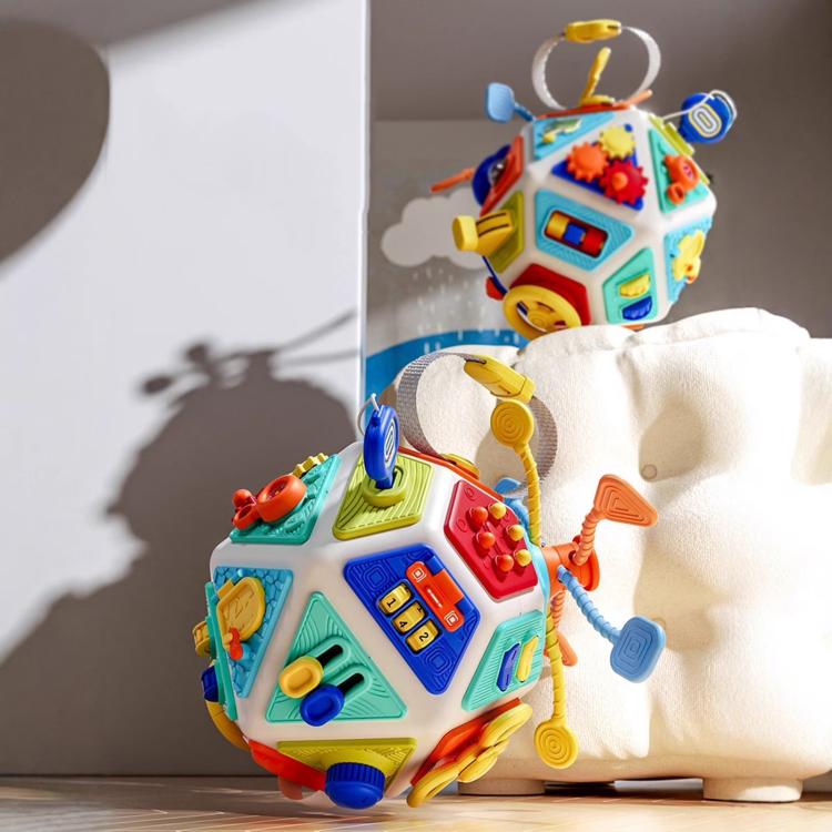 Colorful busy cube toy with dangling strap and activity panels, sitting on a chair