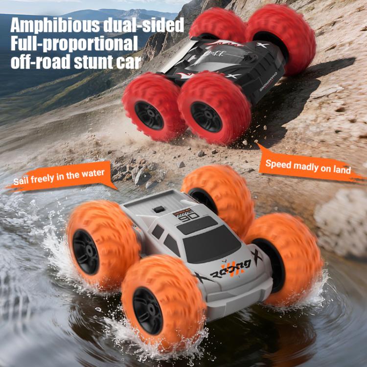 White RC amphibious stunt car with orange wheels splashing in water and on rocks.