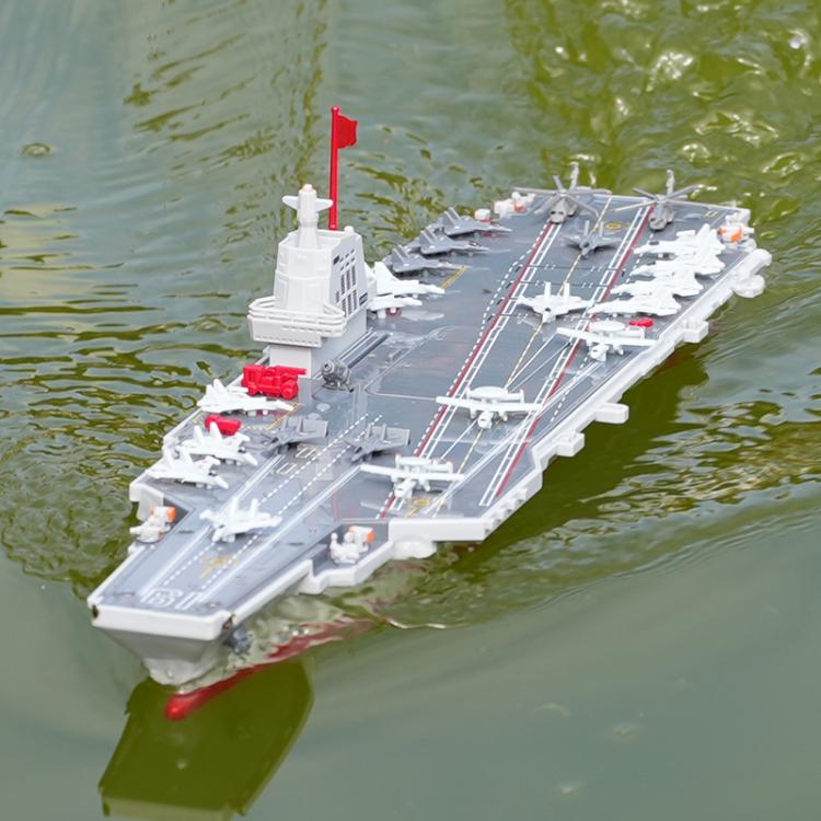 Remote-controlled aircraft carrier toy floating on green water, gray deck and red hull.