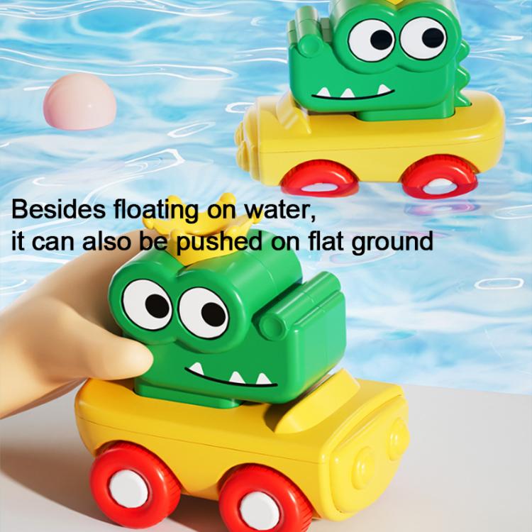 Green crocodile and yellow truck bath toy floats in water, with baby hand visible