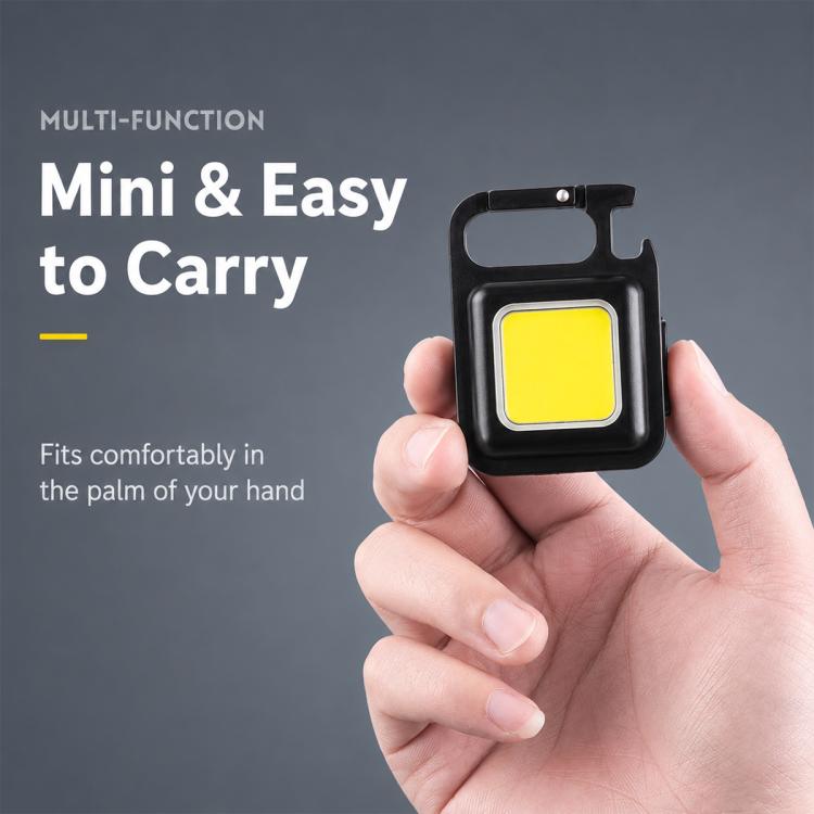 Black mini keychain LED light with yellow COB panel, held in a hand