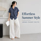 Women’s tie-neck button-front short-sleeve blouse in textured dark blue, worn with casual pants.