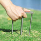 Hand pressing chrome umbrella ground stake prongs into the lawn for stability