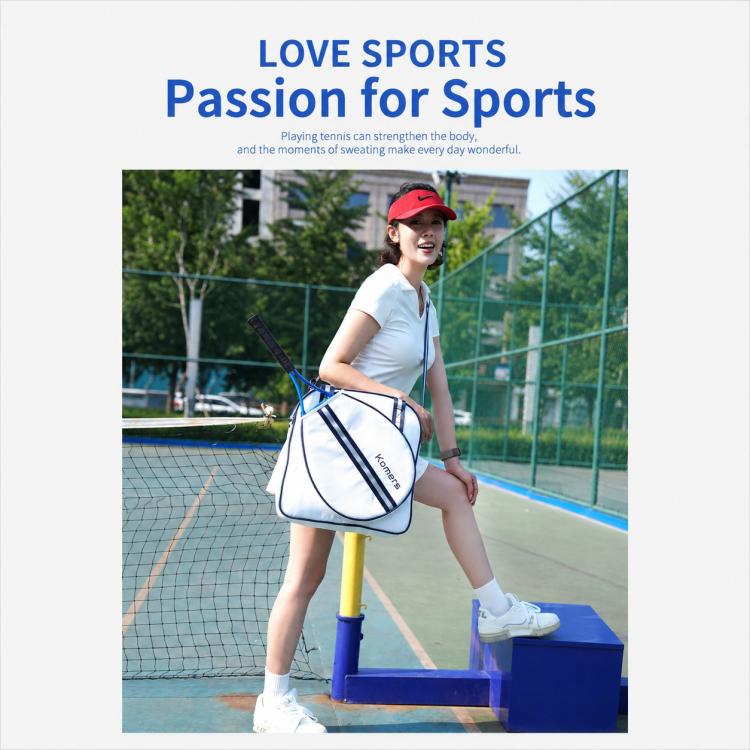 Komers tennis sports bag, white with navy trim, carried by a player at the court.
