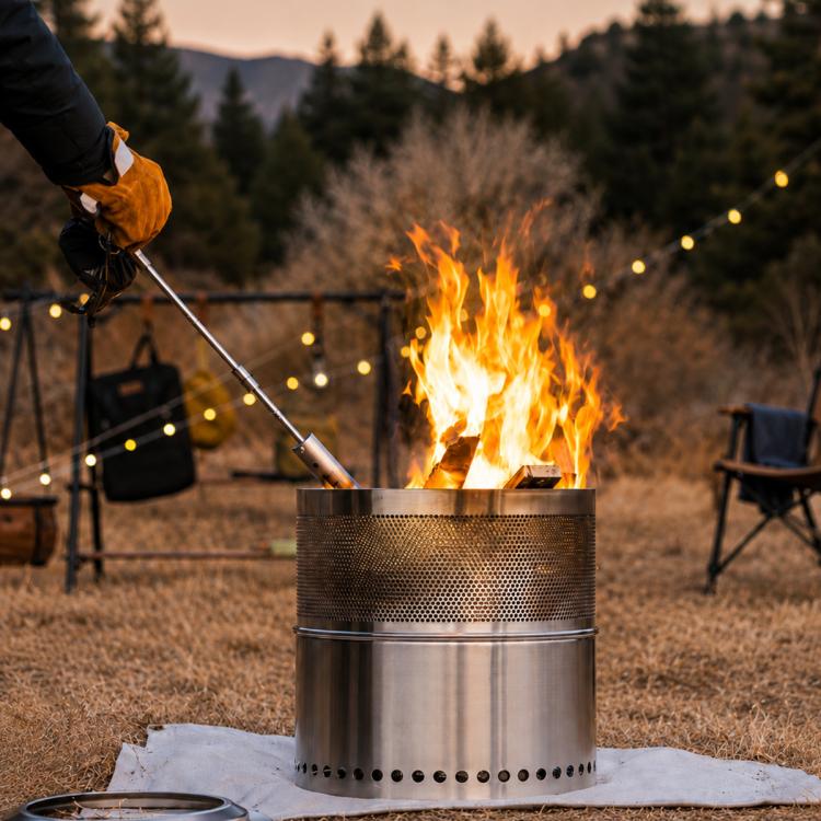 Outdoor camping flame gun with stainless nozzle and wood handle burning over fire pit