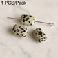 Oval white stone beads with black speckles on wire pin, smooth polished surface