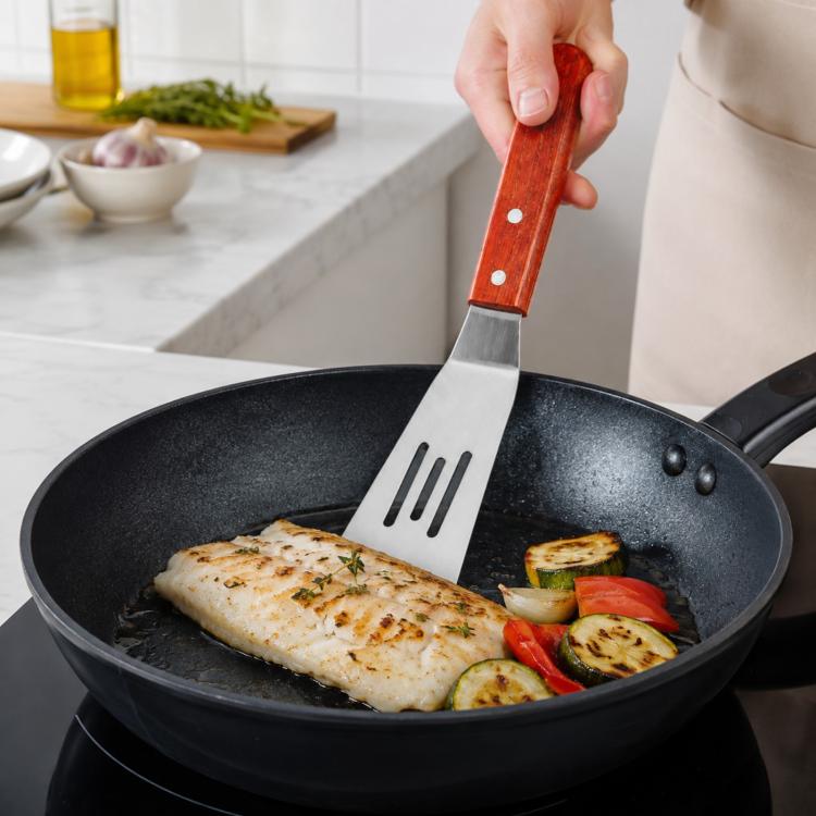 Stainless steel spatula with wooden handle, turning chicken on a nonstick frying pan