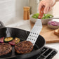 Stainless steel slotted spatula with wooden handle, lifting grilled meat from a skillet