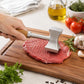 Double-sided meat mallet with textured stainless head striking red meat on a wooden board