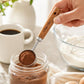Stainless steel measuring cup spoon with wooden handle pouring cocoa powder into a jar