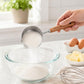 Stainless steel measuring cup spoon with wooden handle filling a glass bowl with flour