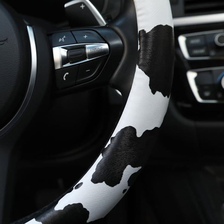 Cow print steering wheel cover grip with black-and-white pattern near control buttons