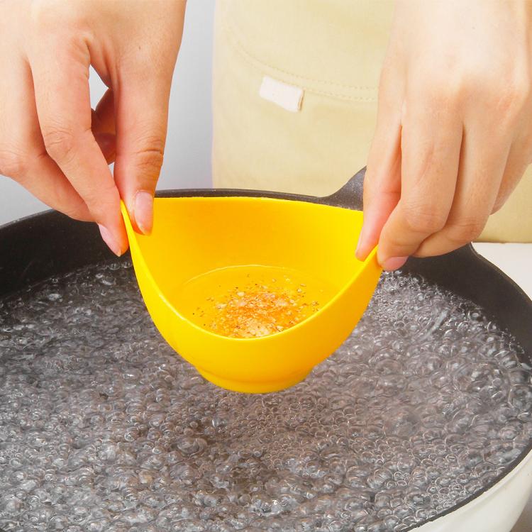 Yellow silicone egg poacher cup held over simmering water by two hands