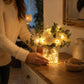 LED faux flower bouquet in lit glass bottle on wooden dresser, white blooms with green leaves