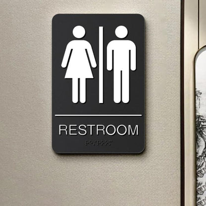 Black restroom Braille sign with restroom icon, raised dots, and RESTROOM label.