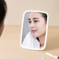 LED makeup mirror reflecting a face, white folding frame and stand