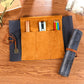 Suede-style pencil bag open with tan slots and blue side pouch; holds pens and dark gray map roll.