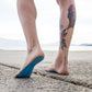 Blue anti-slip summer sandal insoles on barefoot feet on a sandy beach