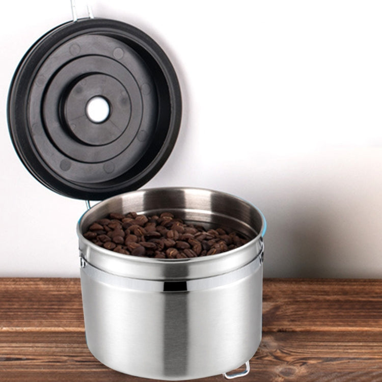 Stainless steel coffee storage container with open lid, latch, and coffee grounds.
