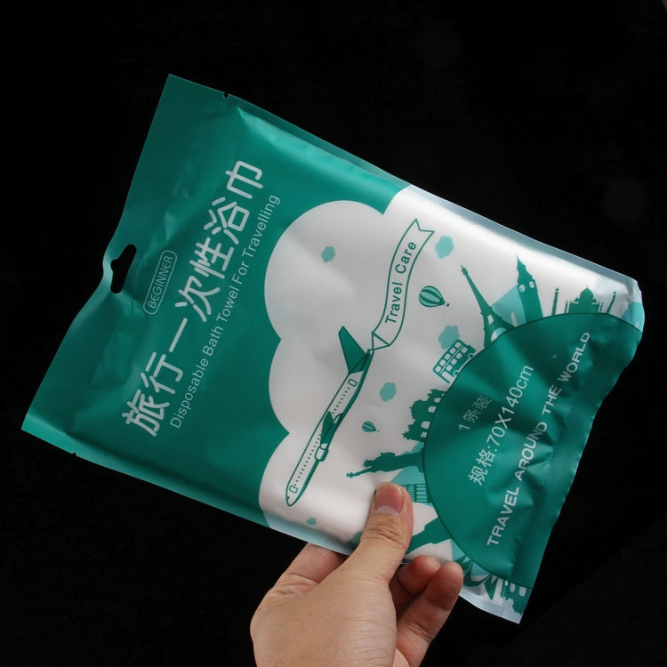 Disposable travel cotton bath towel pouch held in hand, green and white travel graphics