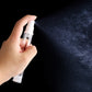 Hand holding a clear airless spray bottle with white fine-mist pump