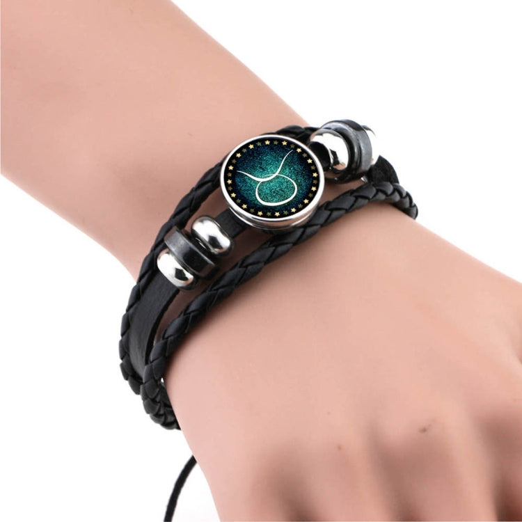Black braided leather bracelet with round teal constellation charm, curved bow glyph, silver clasp