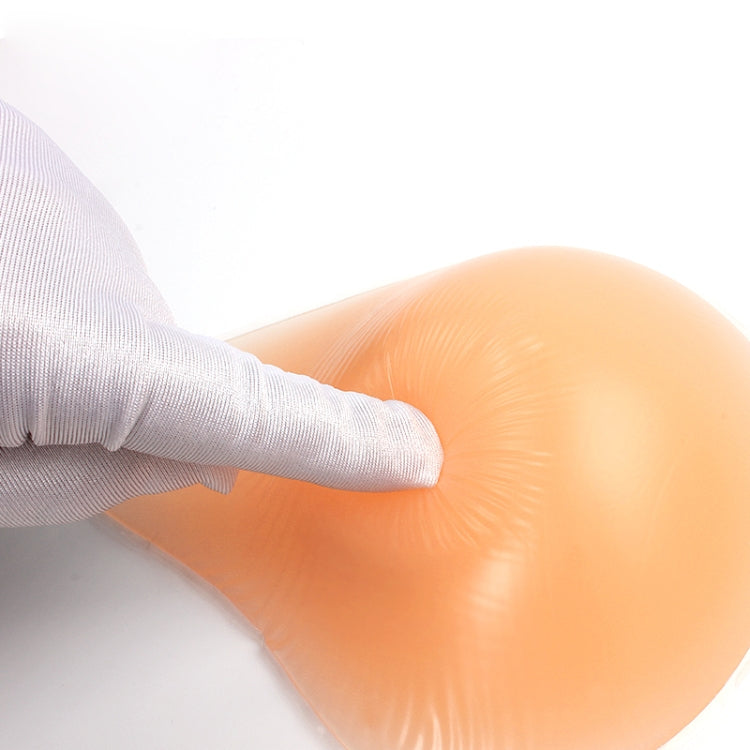 Silicone breast pad being placed by a gloved hand, smooth light peach surface.
