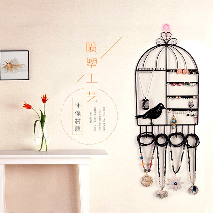 Black birdcage jewelry organizer with hooks and compartments holding necklaces and earrings