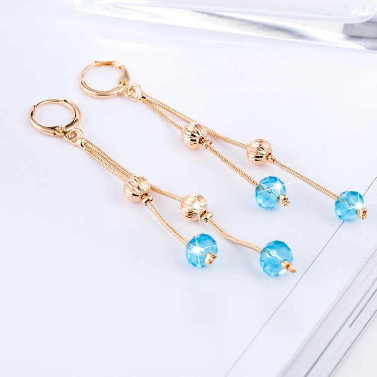 Gold-tone dangling tassel earrings with blue crystal drops on a flat lay