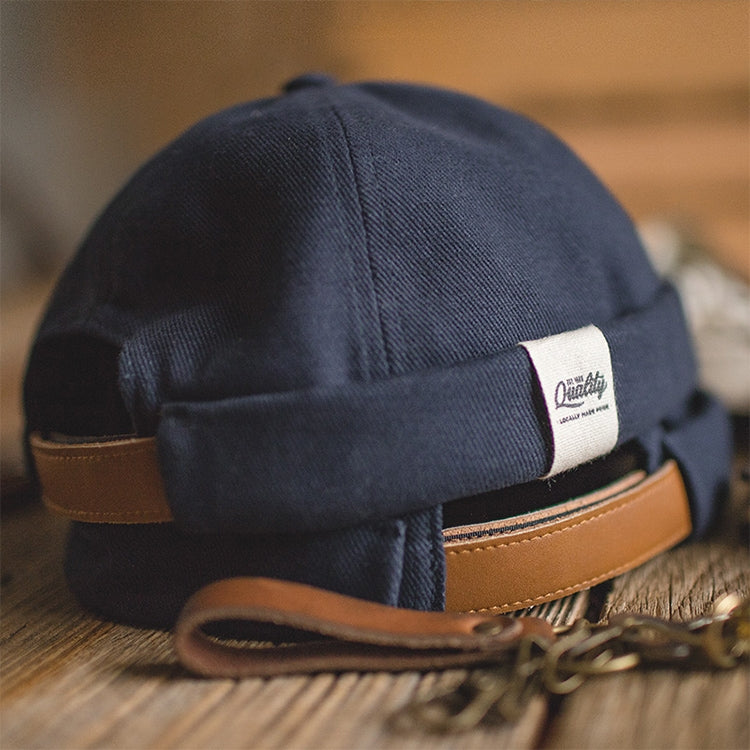 Navy beanie cap with brown leather-style strap and fabric tag on front
