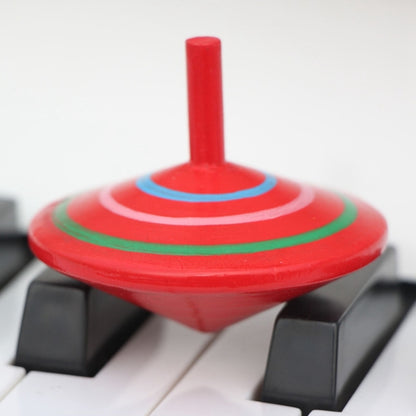 Red wooden rotating gyro top with painted concentric rings and central spindle on blocks