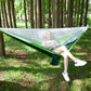 Green and white parachute hammock with mosquito net enclosure, outdoor hanging bed
