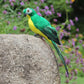 Green simulated parrot ornament perched on a gray stone, long tail visible